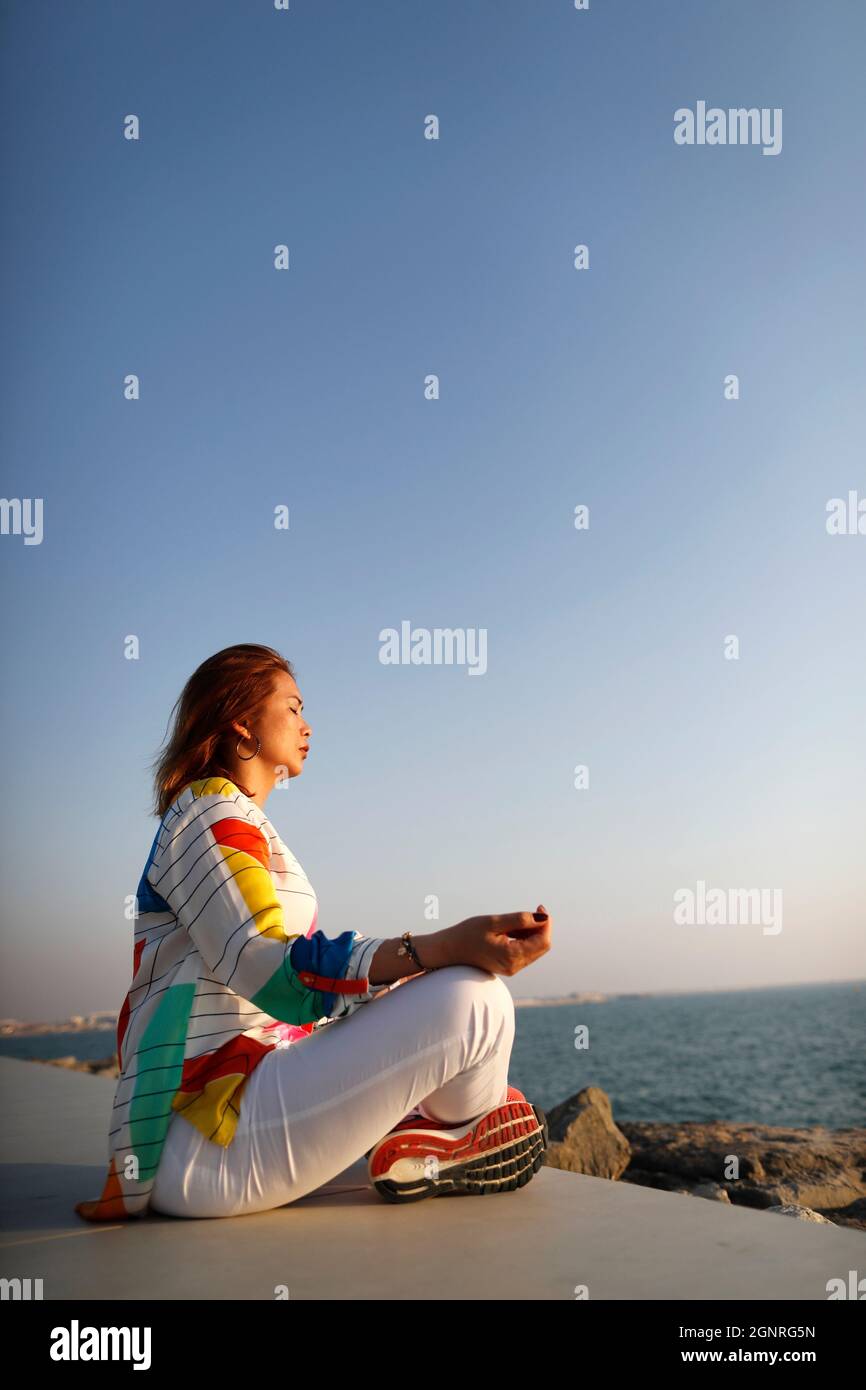 Woman having yoga meditation over the sea before sunset. Silence and relaxation concept. Stock Photo