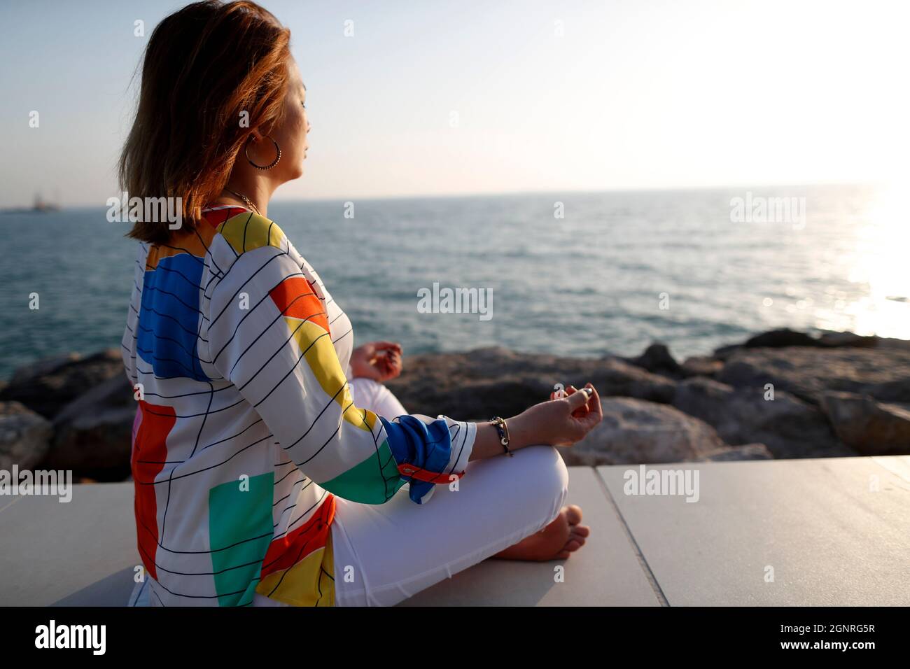 Woman having yoga meditation over the sea before sunset. Silence and relaxation concept. Stock Photo