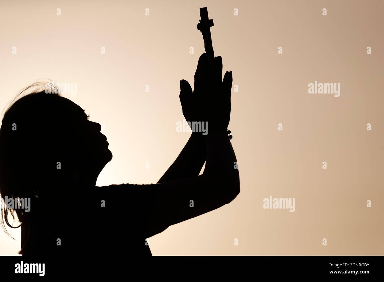 Silhouette of faithful woman praying with chrisrtian cross at sunset ...