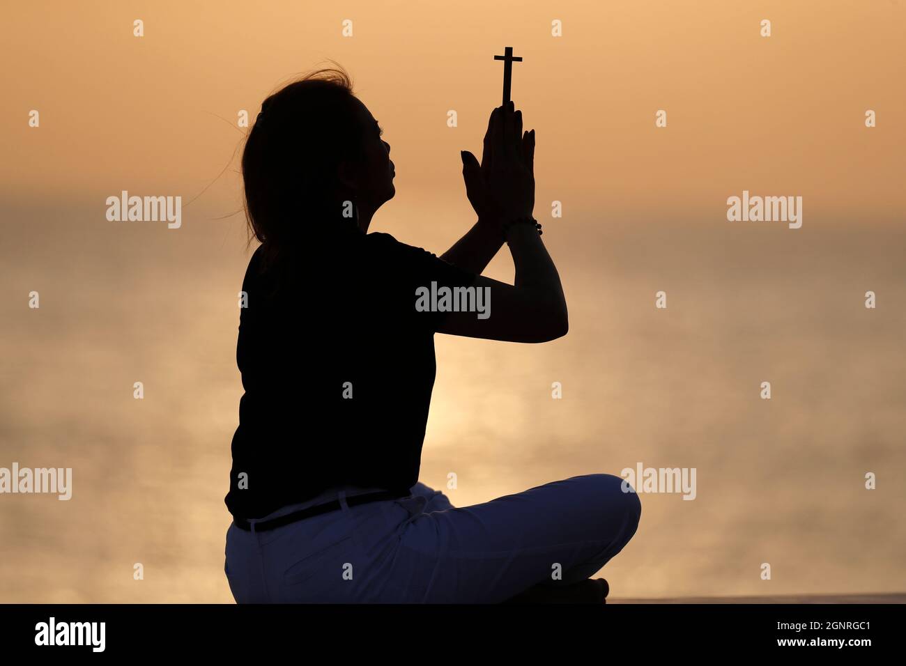 Silhouette of faithful woman praying with chrisrtian cross at sunset ...