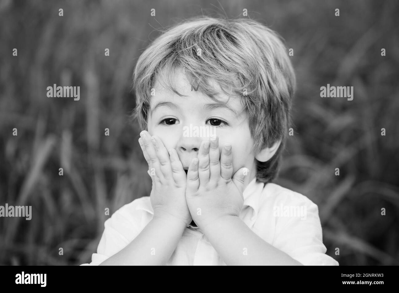 Funny child boy with hands close to face isolated on green background. Child expressing surprise with his hands in his face. Smiling amazed or Stock Photo