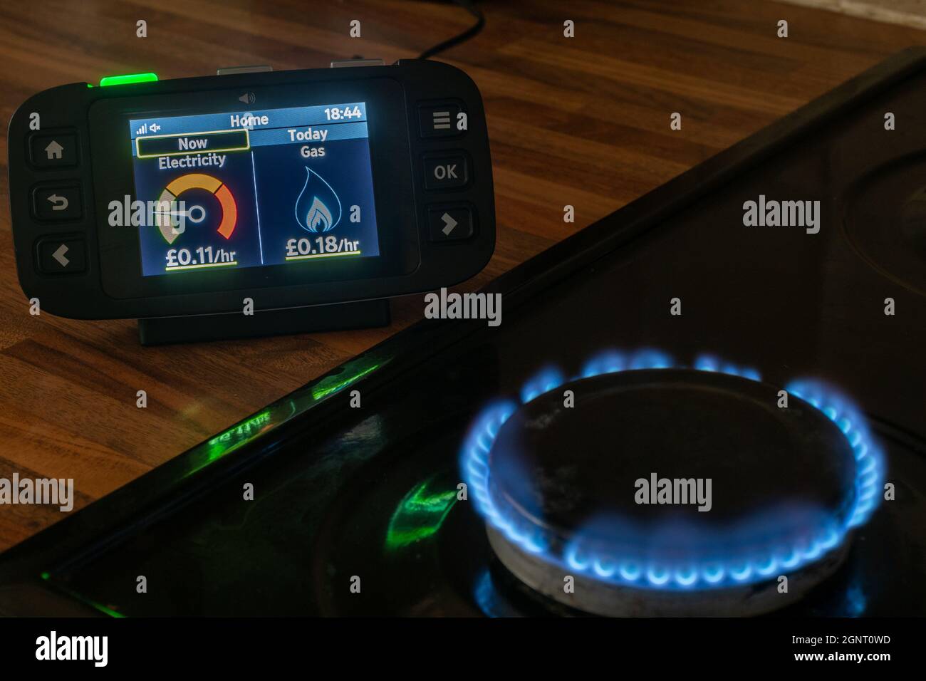 Smart meter readings of gas and electricity usage on a home smart energy monitor next to cooker with gas hob flame Stock Photo