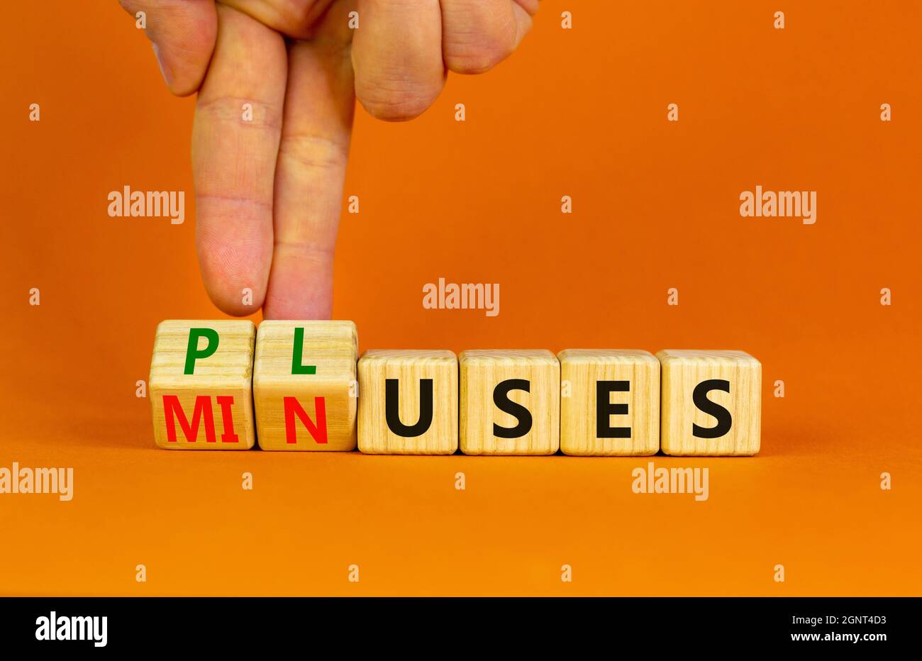 Pluses and minuses symbol. Businessman turns wooden cubes and changes the word 'minuses' to 'pluses'. Beautiful orange table, orange background. Busin Stock Photo