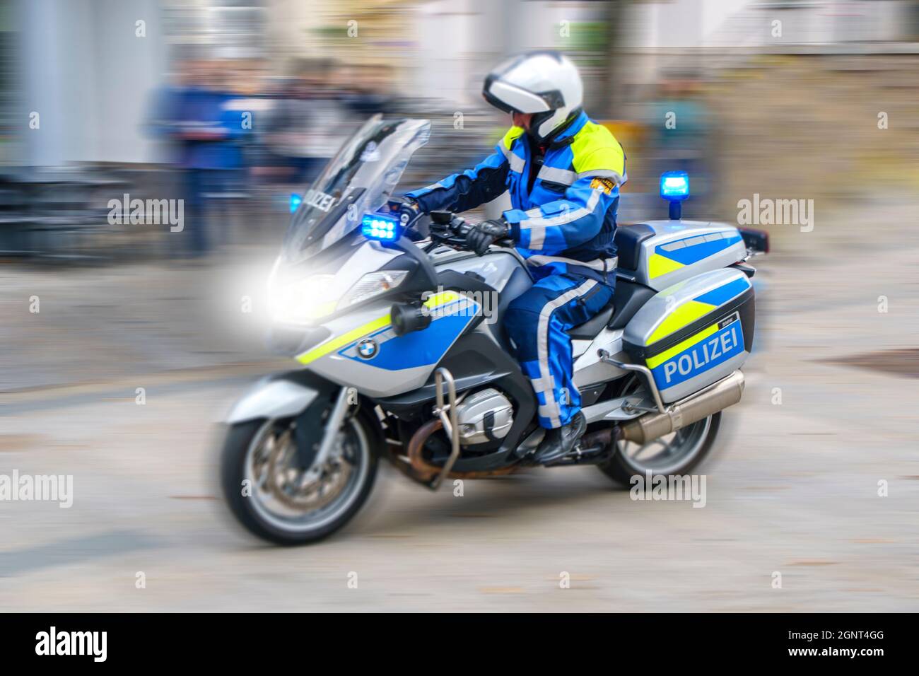 Ein Polizeimotorrad fährt mit hoher Geschwindigkeit und Blaulicht durch die Stadt Augsburg Stock Photo