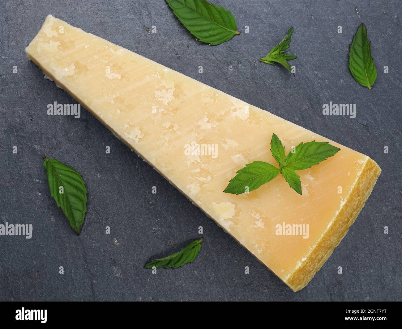 Top view of piece of parmigiano reggiano or parmesan cheese on dark slate plate with green mint leaves Stock Photo