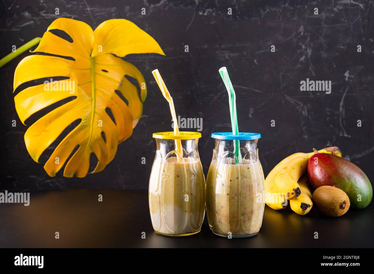 Two glasses of fruit cocktail. Two glasses with straws. Fruit and cocktail on a black background. Tropical fruits in a bowl. Stock Photo