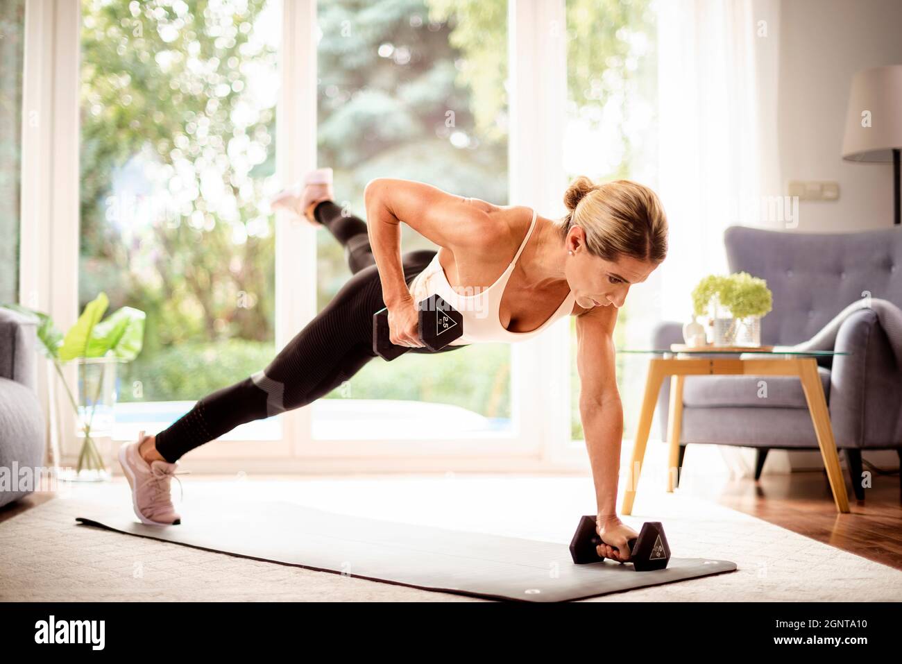Shot of a woman using dumbbells while doing body workout at home. Woman  wearing sports wear while exercising on the yoga mat. Healthy lifestyle  Stock Photo - Alamy