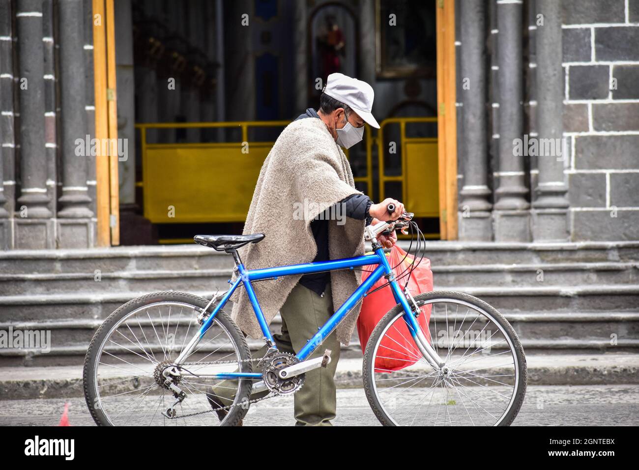 A men with a bycicle pases by the Cumbal church wearing a protective face mask against COVID-19 in Cumbal - Nariño, Colombia on August 15, 2021. Stock Photo