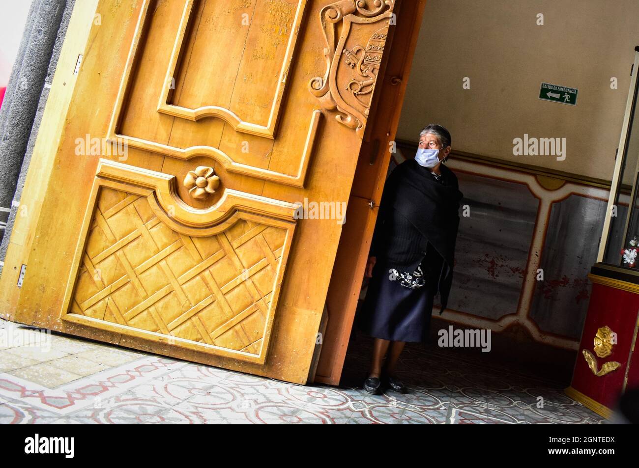 A women who works in the Cumbal primary church sees passerby pass as she uses a protective face mask against COVID-19 in Cumbal - Nariño, Colombia on August 15, 2021. Stock Photo