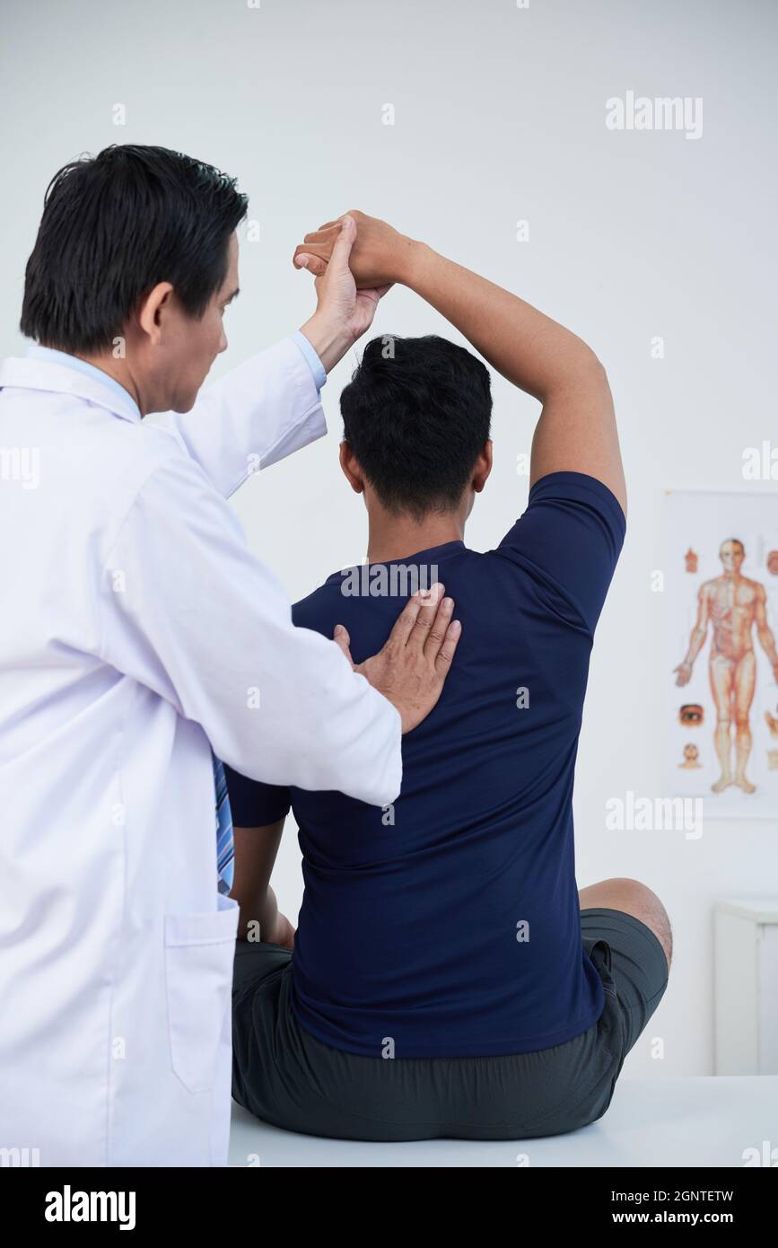Vertical medium back view shot of modern mature osteopathic therapist treating young man manipulating his bones, muscles and fasciae Stock Photo