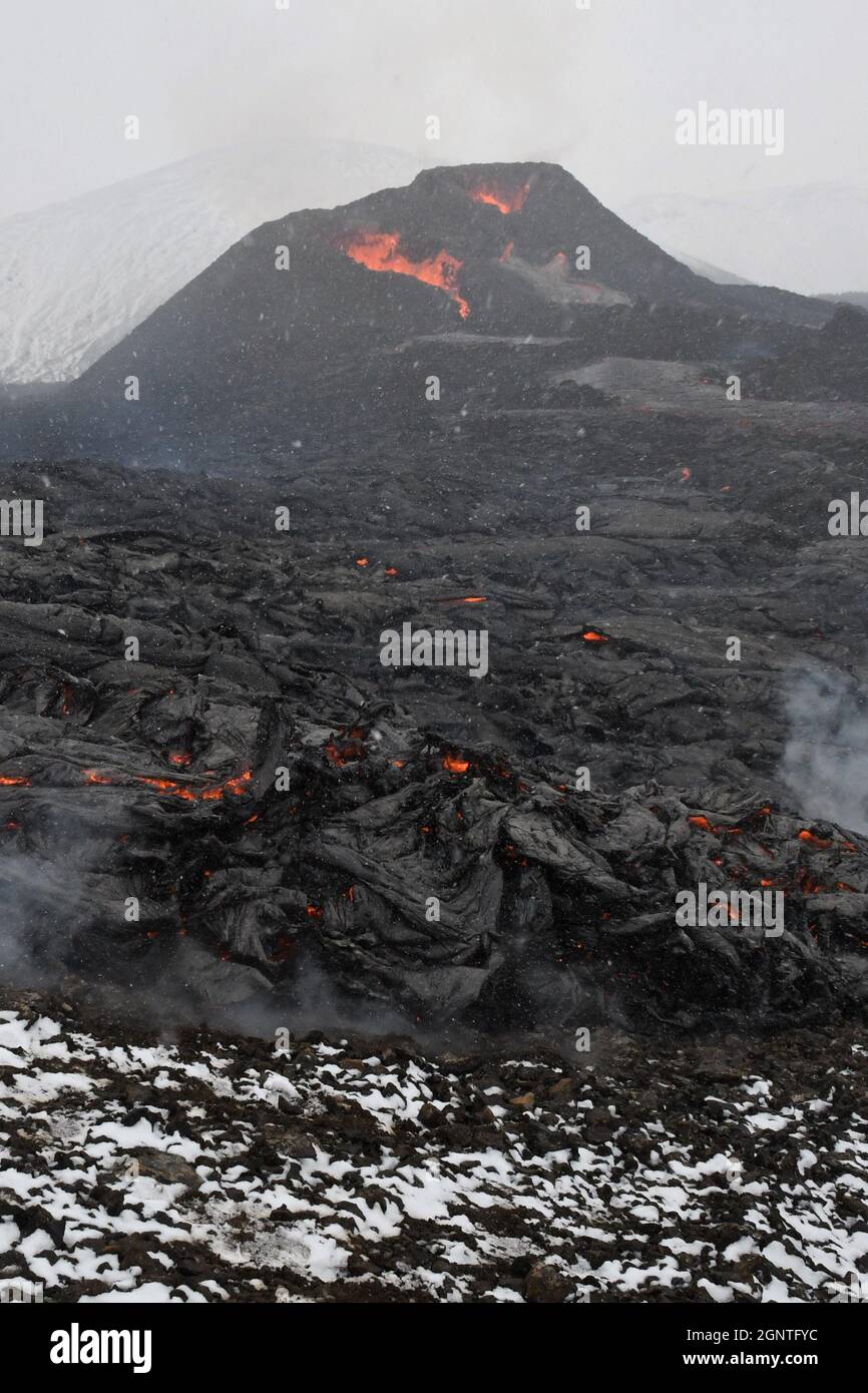 Two vents at Fagradalsfjall volcanic eruption, Iceland. Crusted black lava is in the foreground, with some patches of molten red lava and steam rising Stock Photo