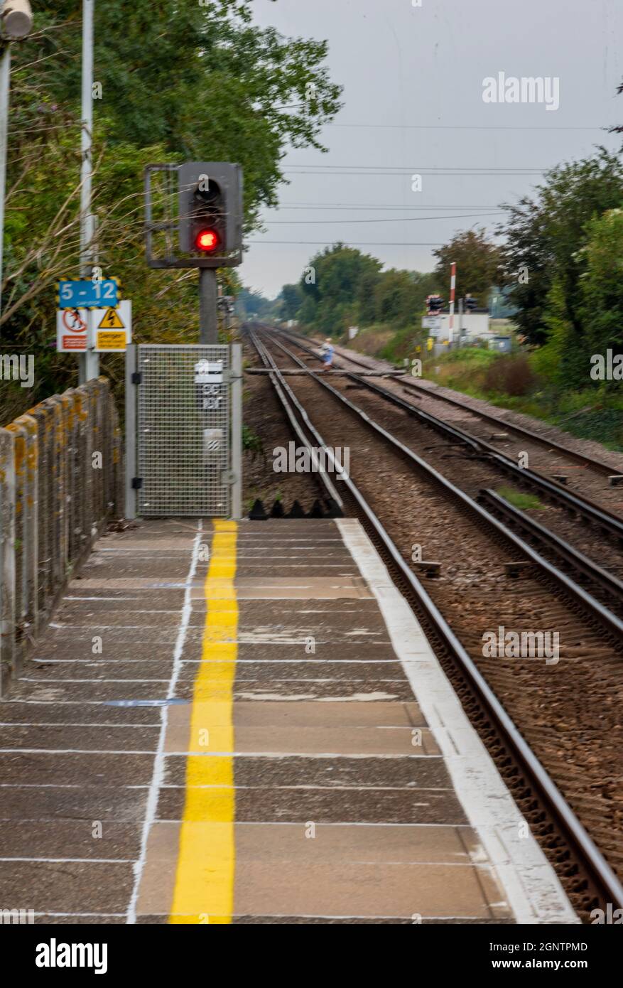 Railway trains station platform and rail tracks with a red signal at the end of the platform and lines tapering to a vanishing or disappearing point Stock Photo