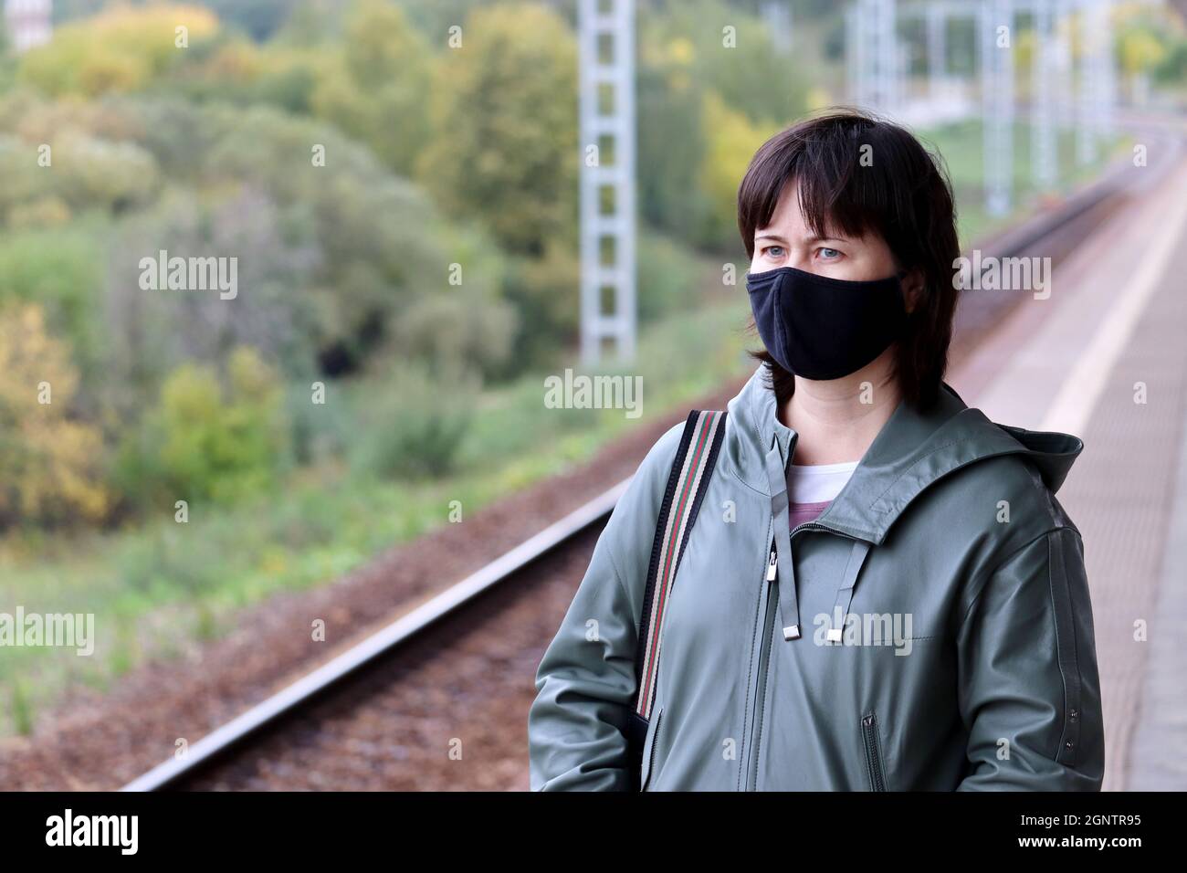 Woman in black mask waiting a train on a railroad station. Safety measures on public transport during covid-19 pandemic Stock Photo