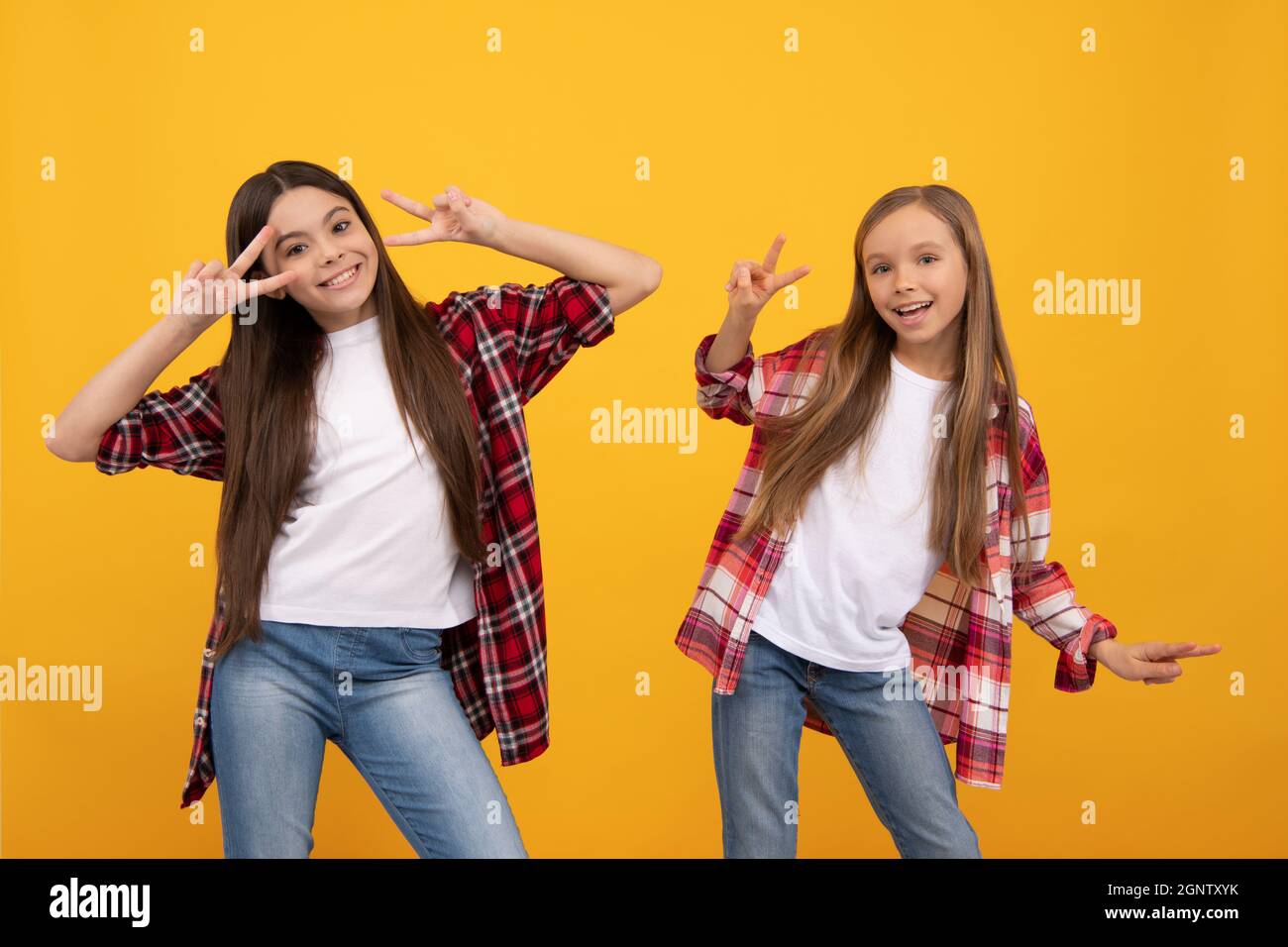 happy teen girls in casual shirt having fun showing peace gesture on yellow background, childhood. Stock Photo