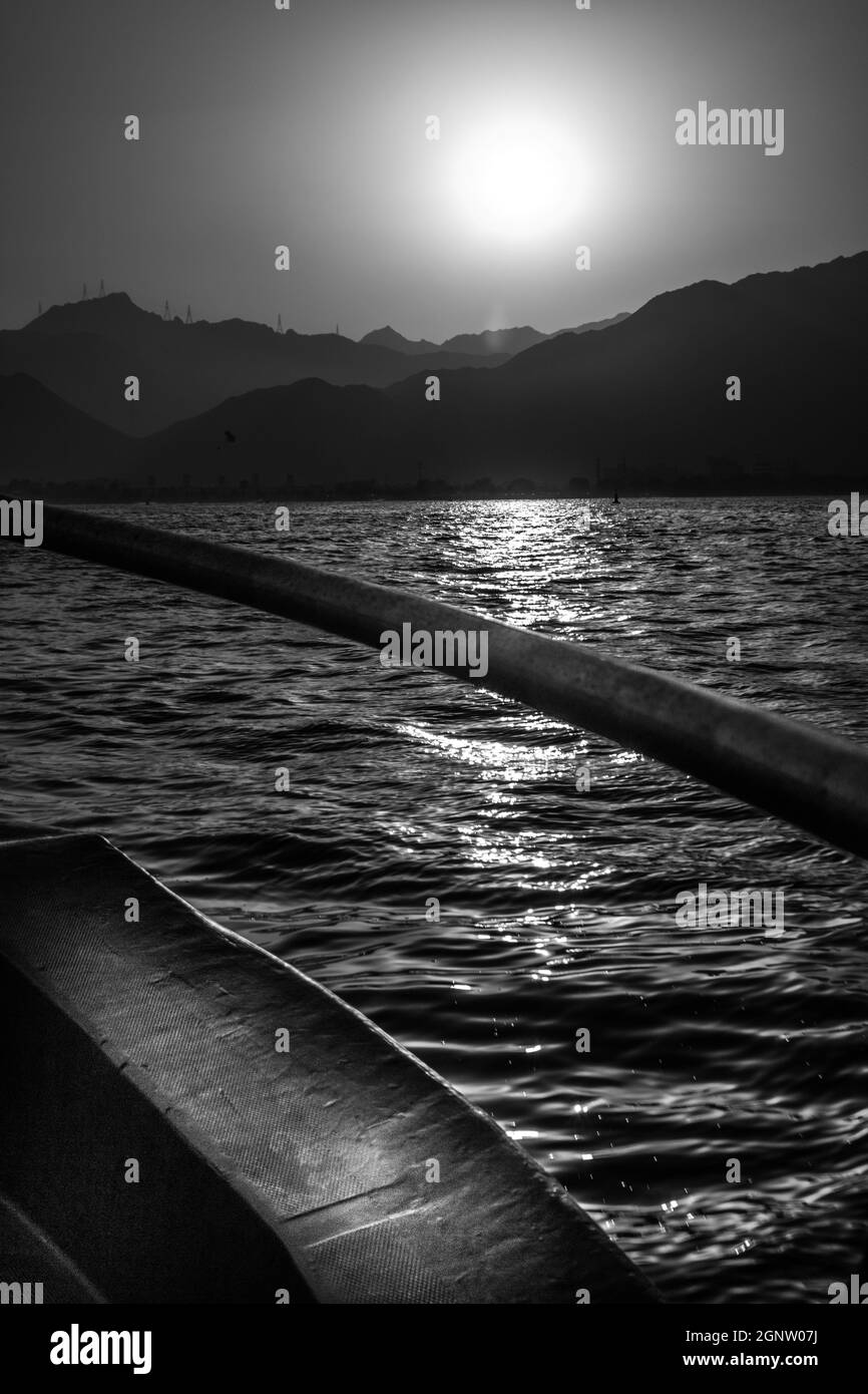 Black and white view from a boat of a sunset over hills and a sea Stock Photo