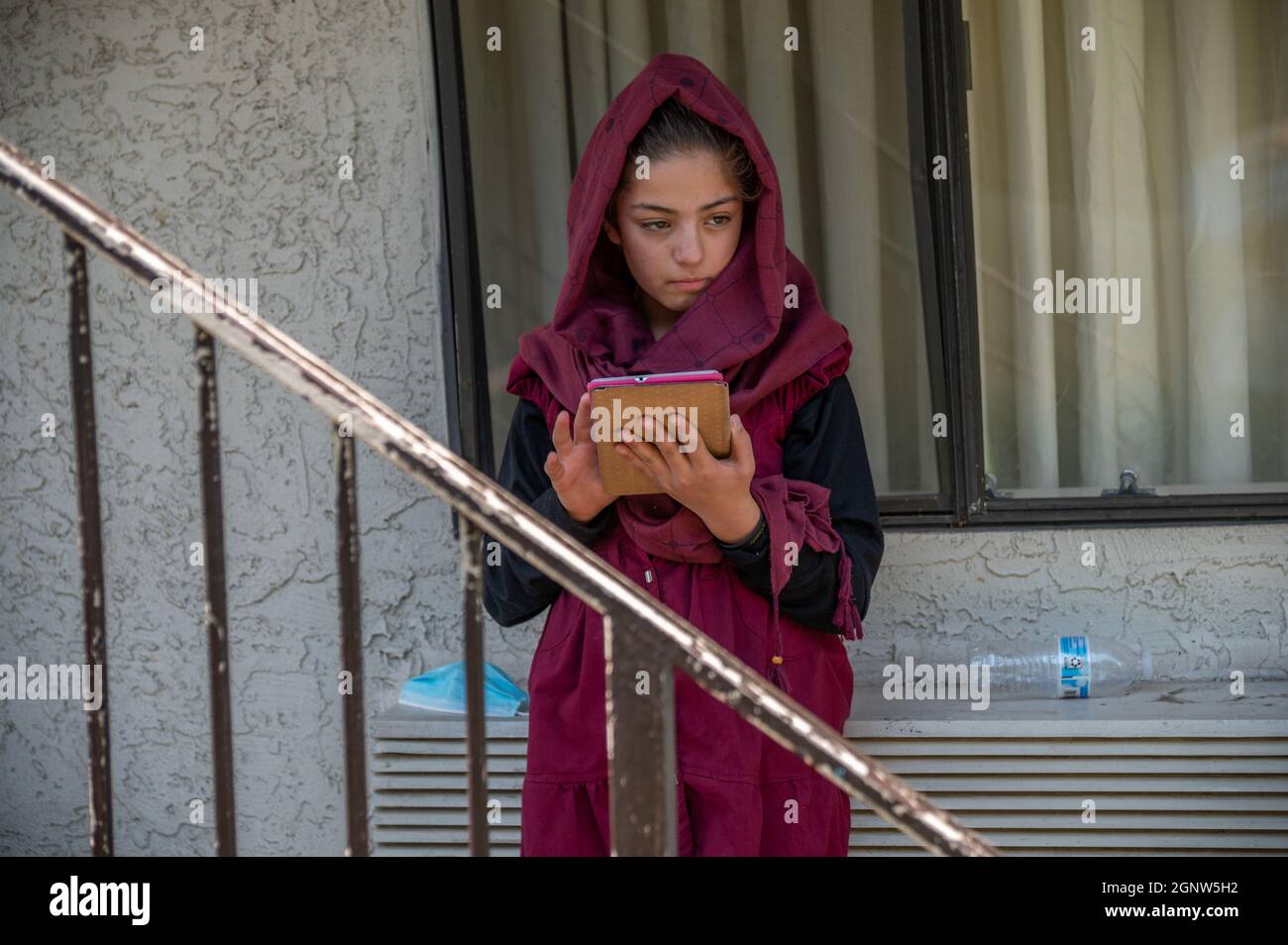 Sacramento, CA, USA. 25th Aug, 2021. Behind a worn banister at America's Best Value Inn in North Highlands, Afghan refugee Zulaikha, 13, plays on a tablet, a few days after arriving in the United States. Her father Abdul said the family will enroll their children in school once they are vaccinated. (Credit Image: © Renée C. Byer/ZUMA Press Wire) Stock Photo