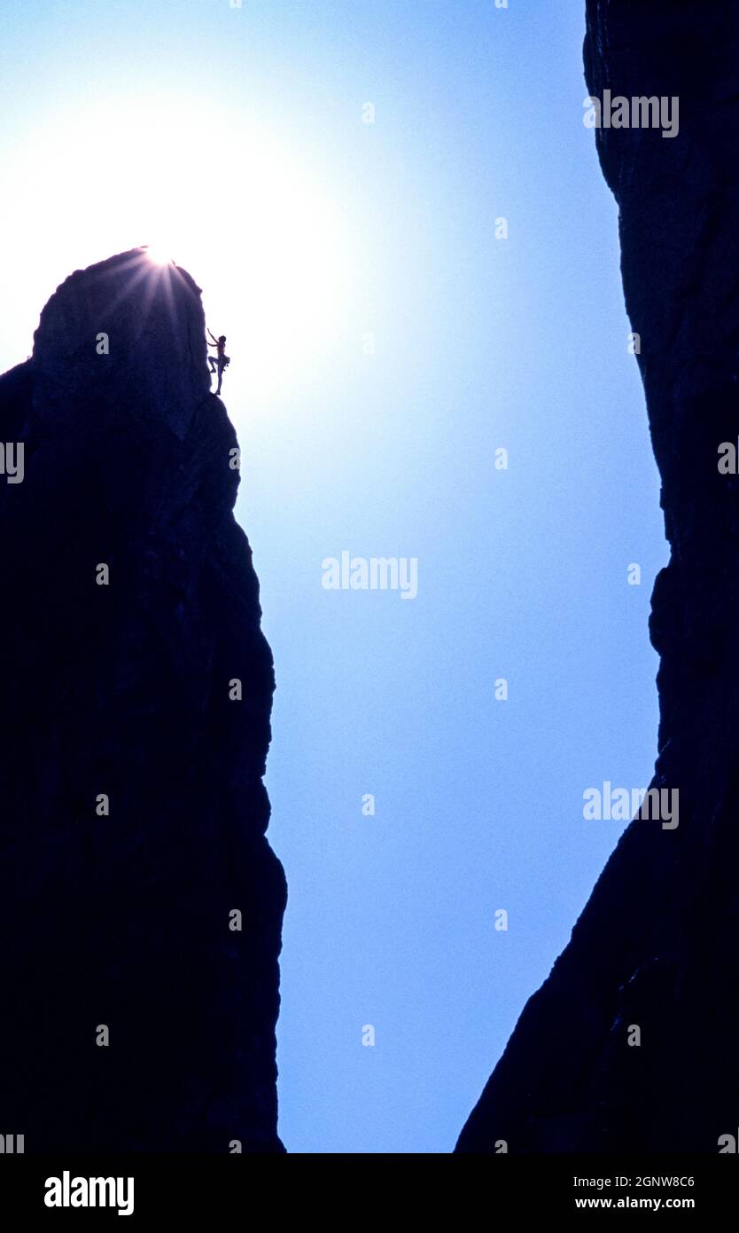 A female climber nearing the top of a rock formation where the sun is peaking over. Stock Photo