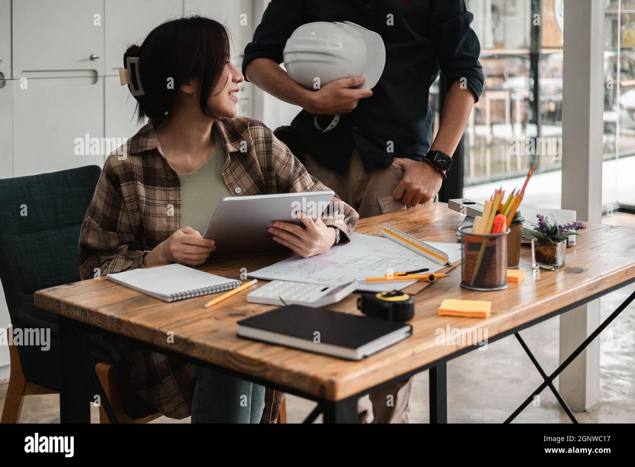 Two colleagues discussing data working with digital tablet for architectural project at construction site at desk in office. Stock Photo