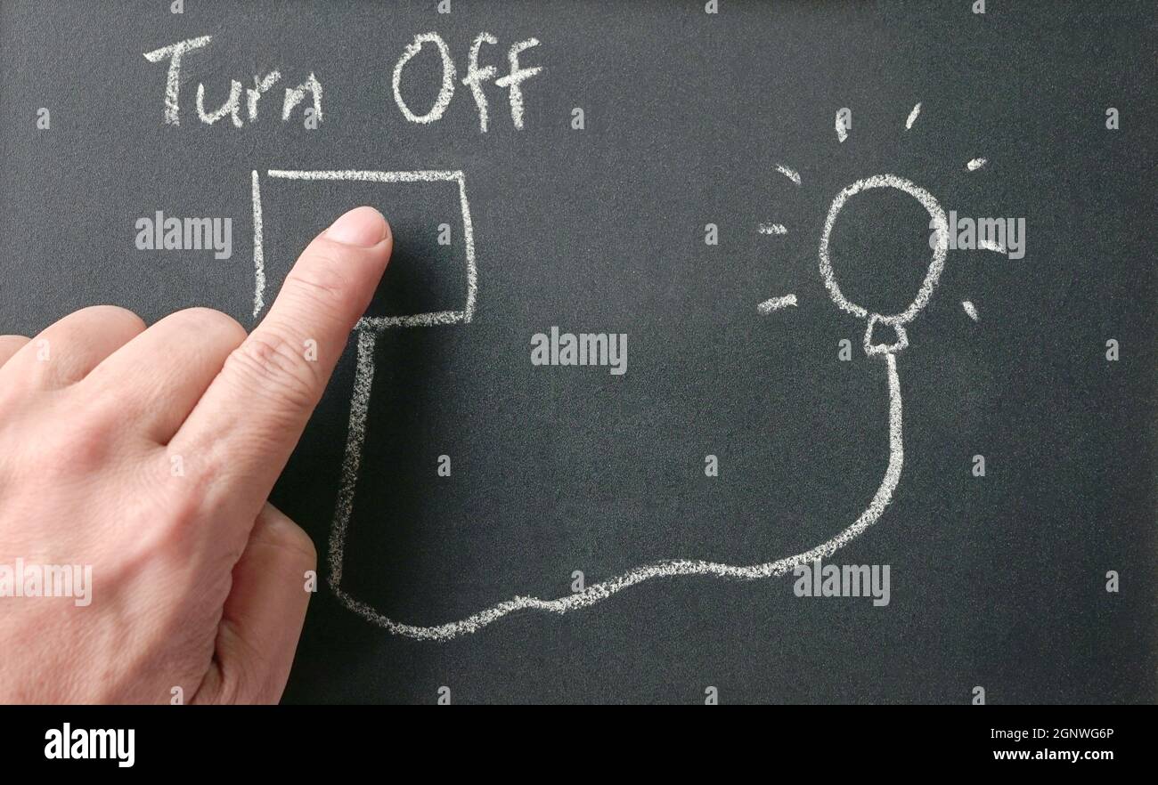 Man's finger on drawing of power outlet that connects power to light bulb on blackboard with words, turn off. Save energy concept. Stock Photo