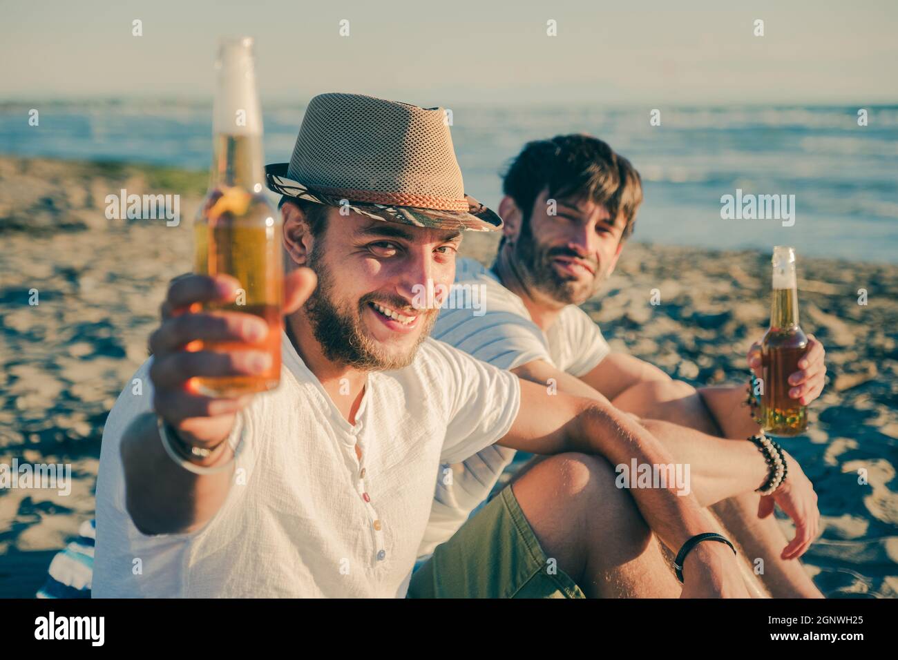 Portrait of friends having a rest on the beach drinking beer. Cheerful young people spending nice time together while sitting on the beach and smiling Stock Photo