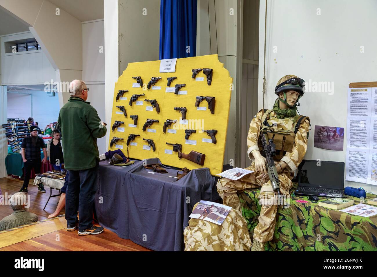 Displays at an arms and militaria show. A man looks at a collection of WWI pistols. Sitting alongside is a mannequin in an Afghanistan War uniform Stock Photo