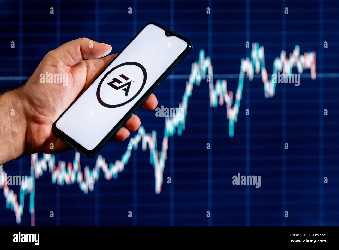 A smartphone with the Electronic Arts logo in a hand. Stock chart on the background. Stock Photo