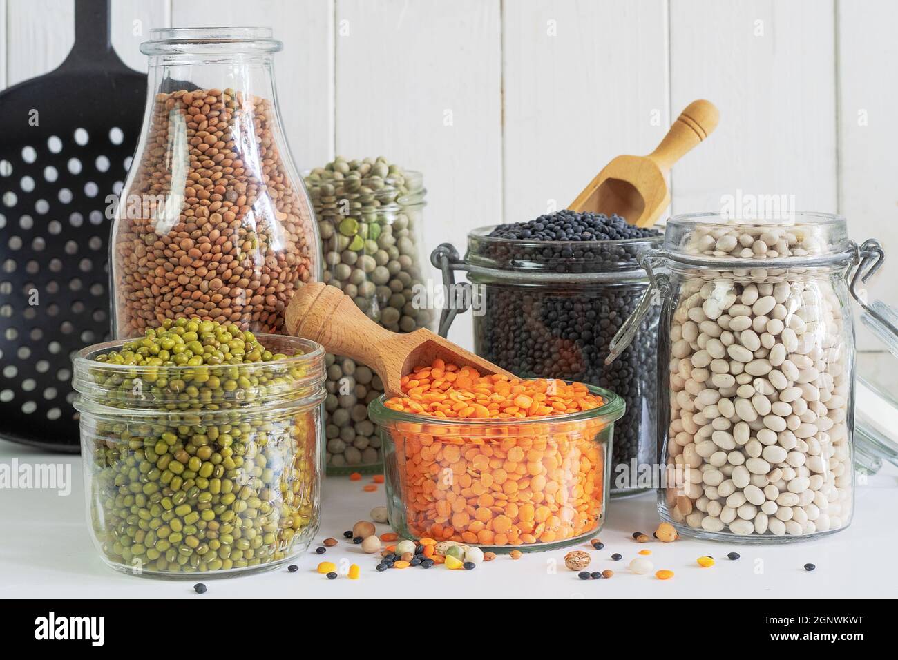 Assortment of colorful legumes in jars and glasses on a light kitchen table Stock Photo