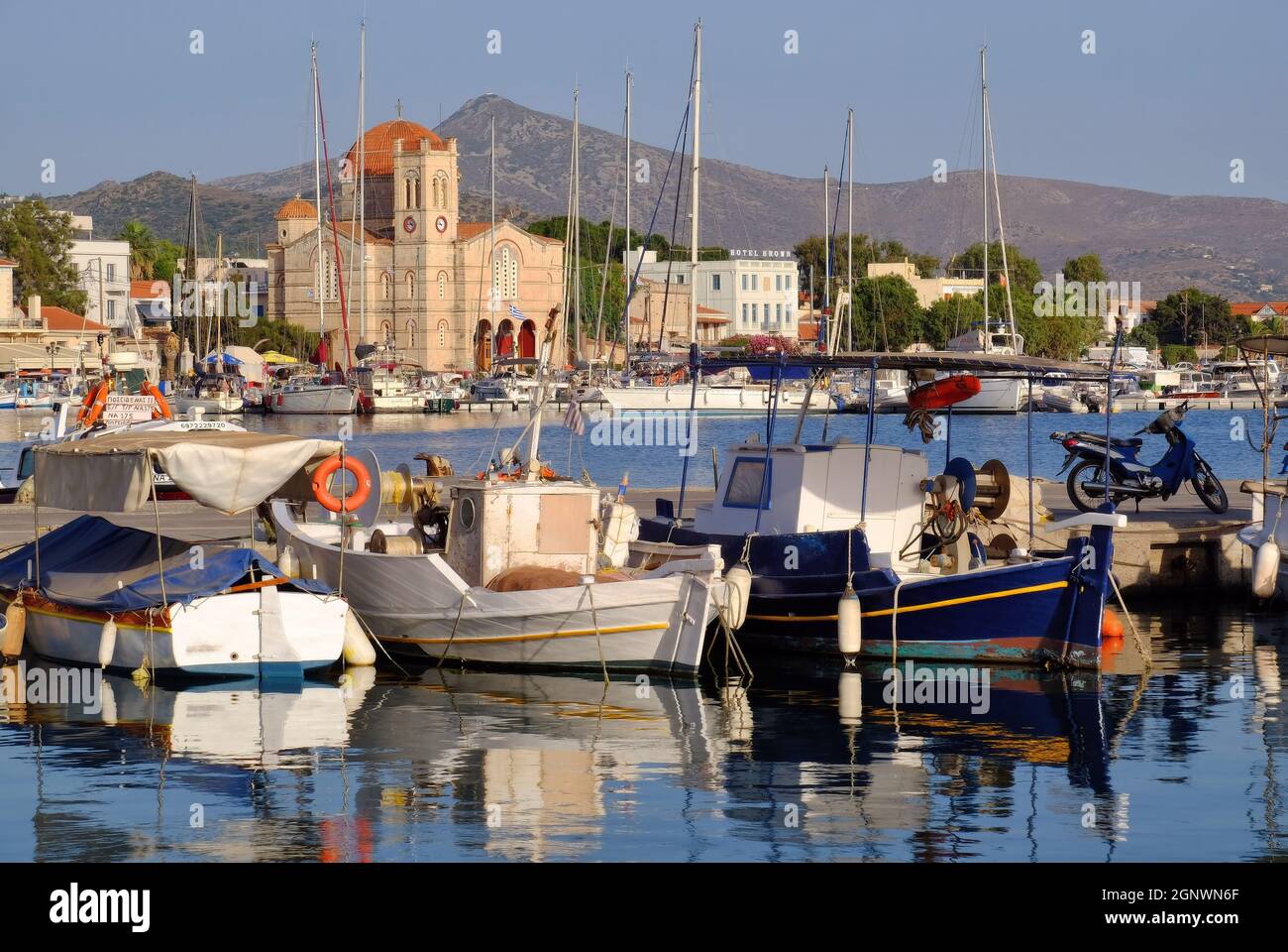 Church Isodia Theotokou, hills, fishing boats and reflections in the port soon before sunset at Aegina town, Egina Island, Greece Stock Photo