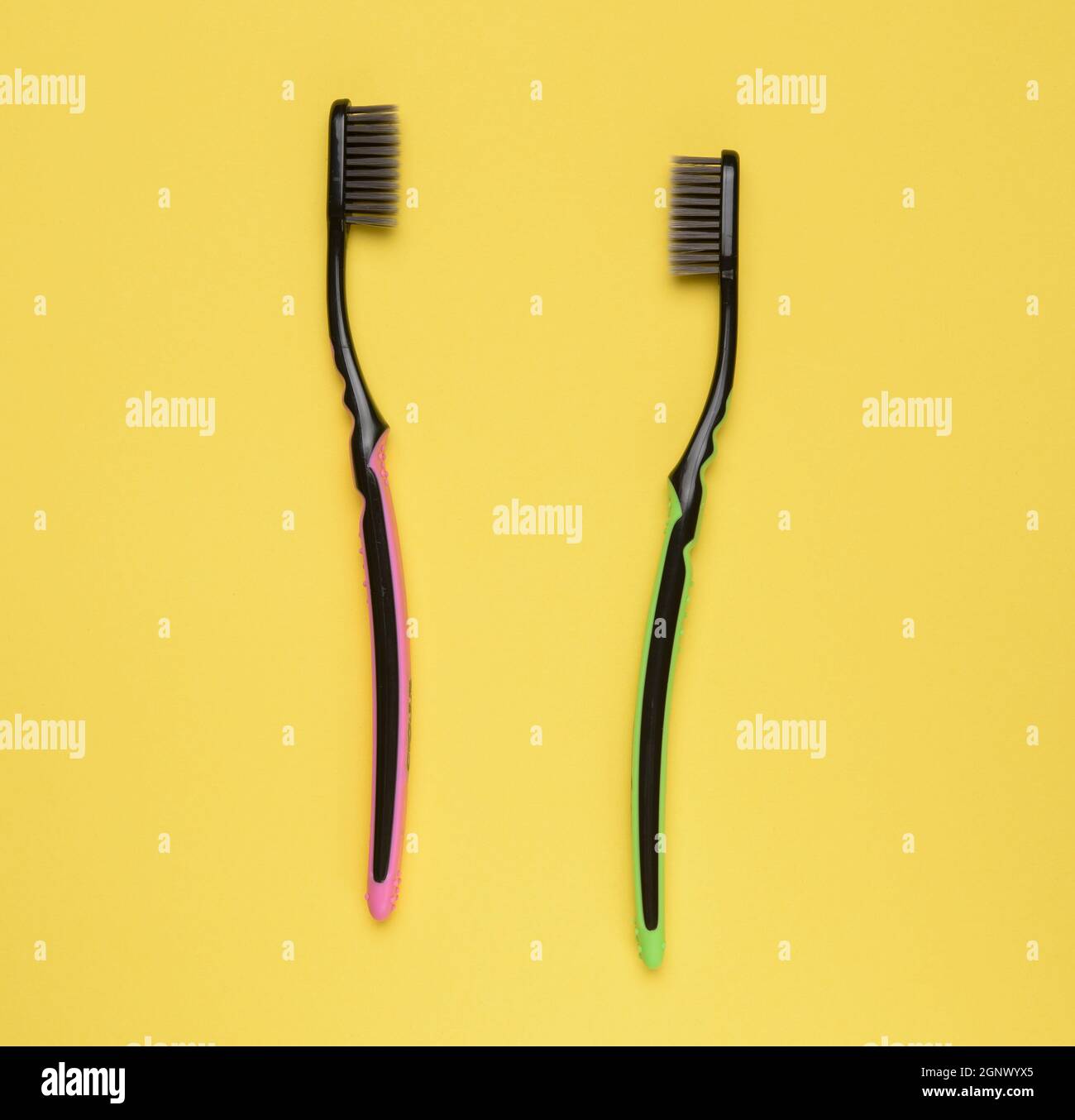 pink and green plastic toothbrushes on a yellow background, top view ...