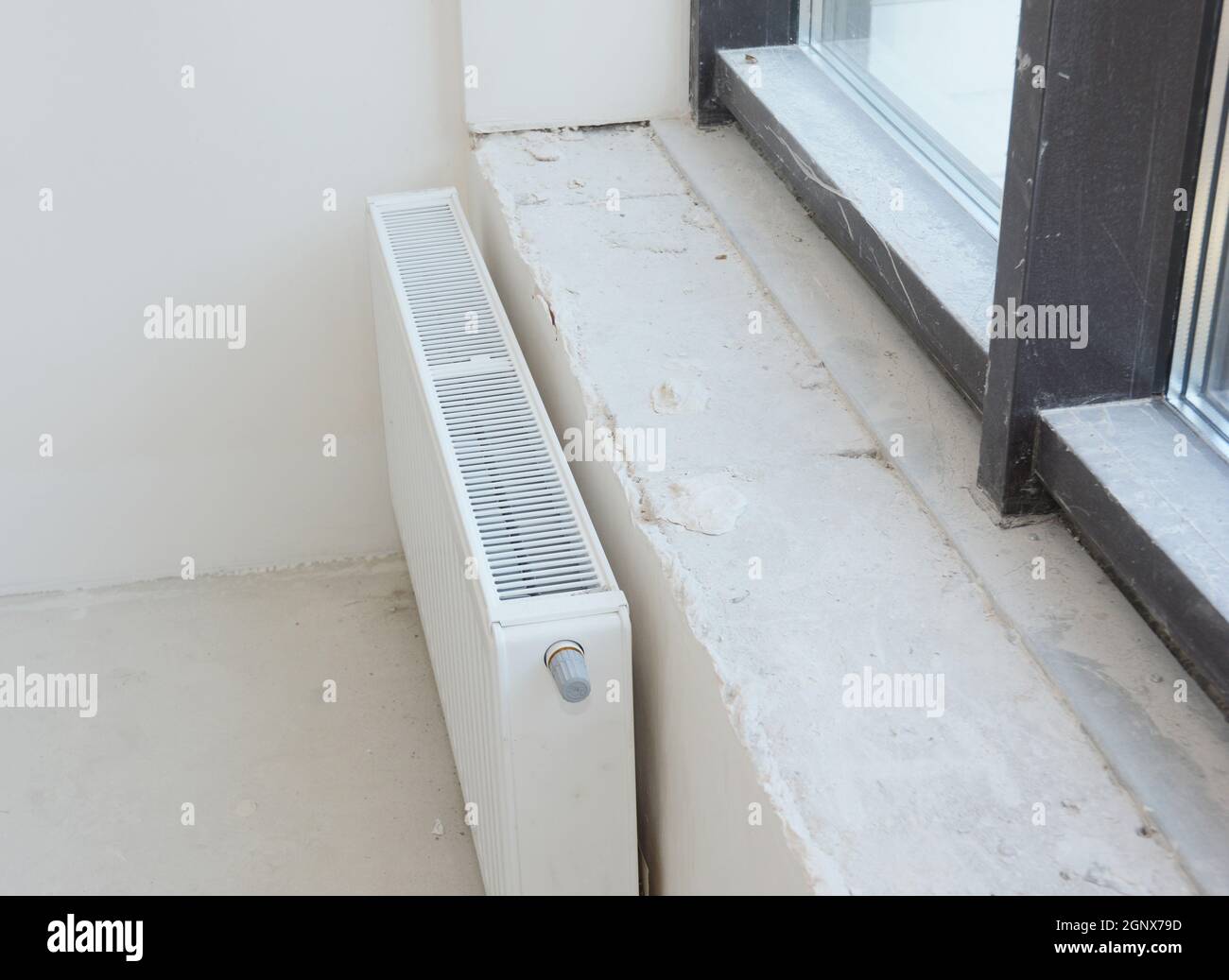 Installing metal white radiator heating with thermostat in new house construction. Stock Photo