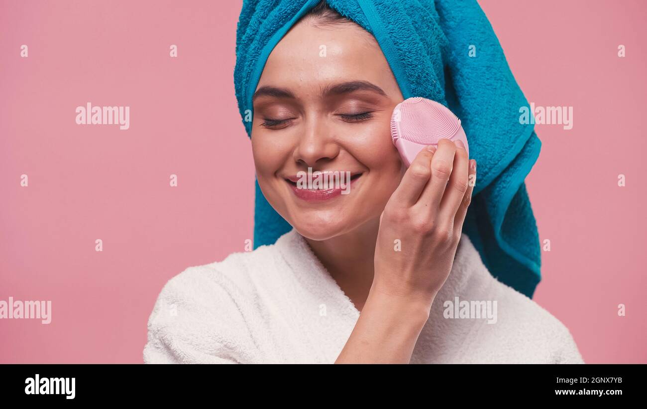 joyful woman using silicone facial cleanser with closed eyes isolated on pink Stock Photo