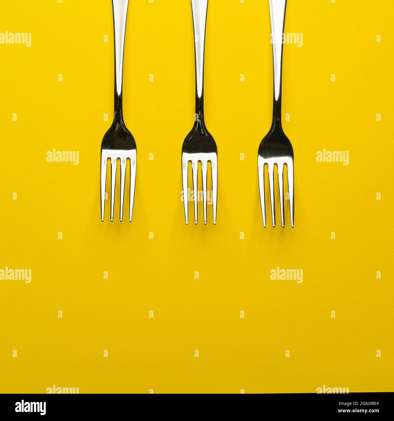 three forks arranged on a yellow surface Stock Photo Alamy
