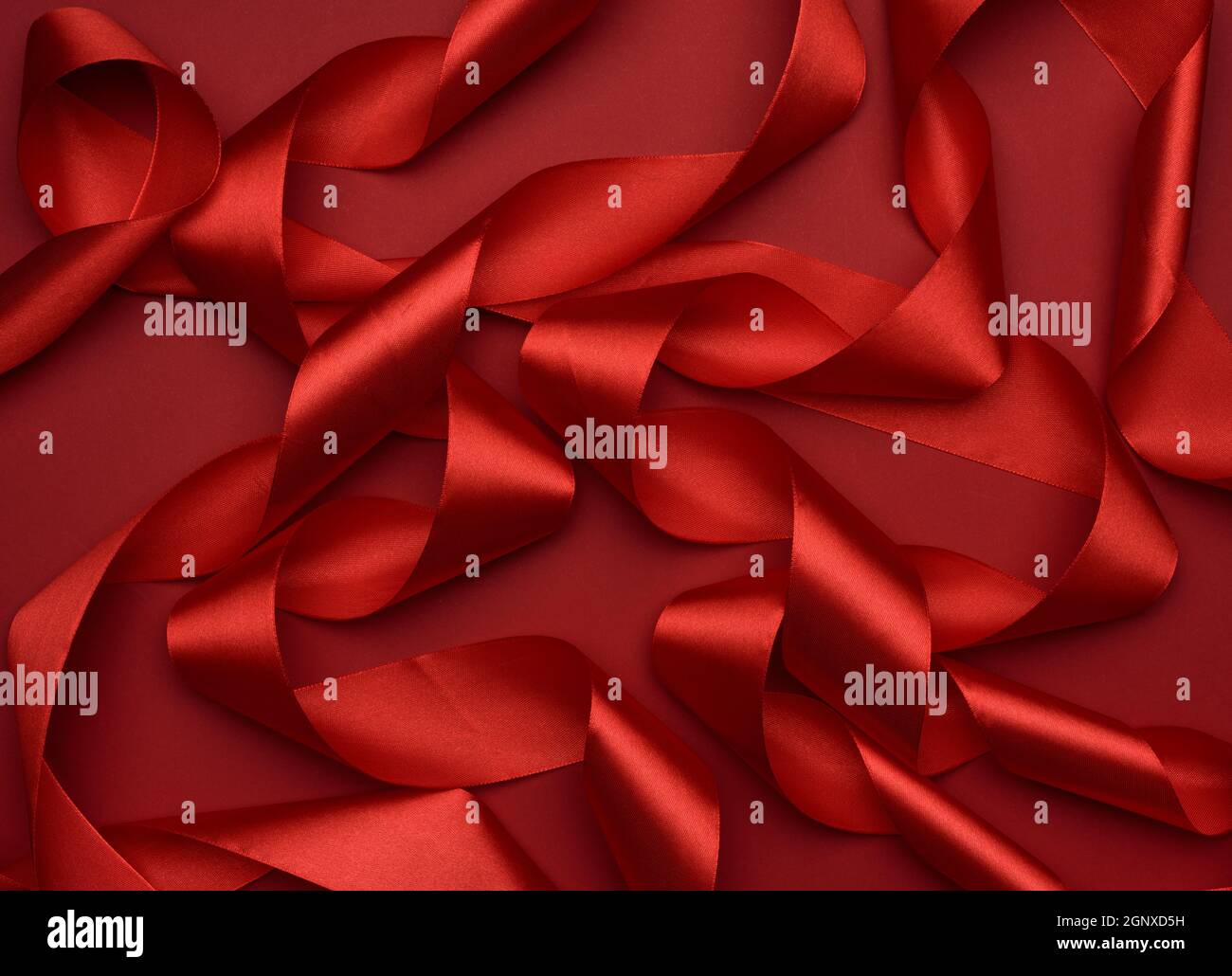 curled red silk ribbon on a red background, festive background Stock Photo