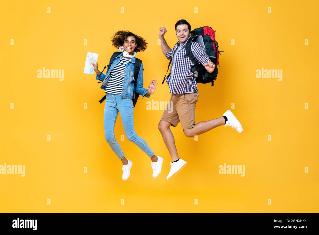 Happy young interracial tourist couple with backpacks ready to travel jumping in yellow color background Stock Photo