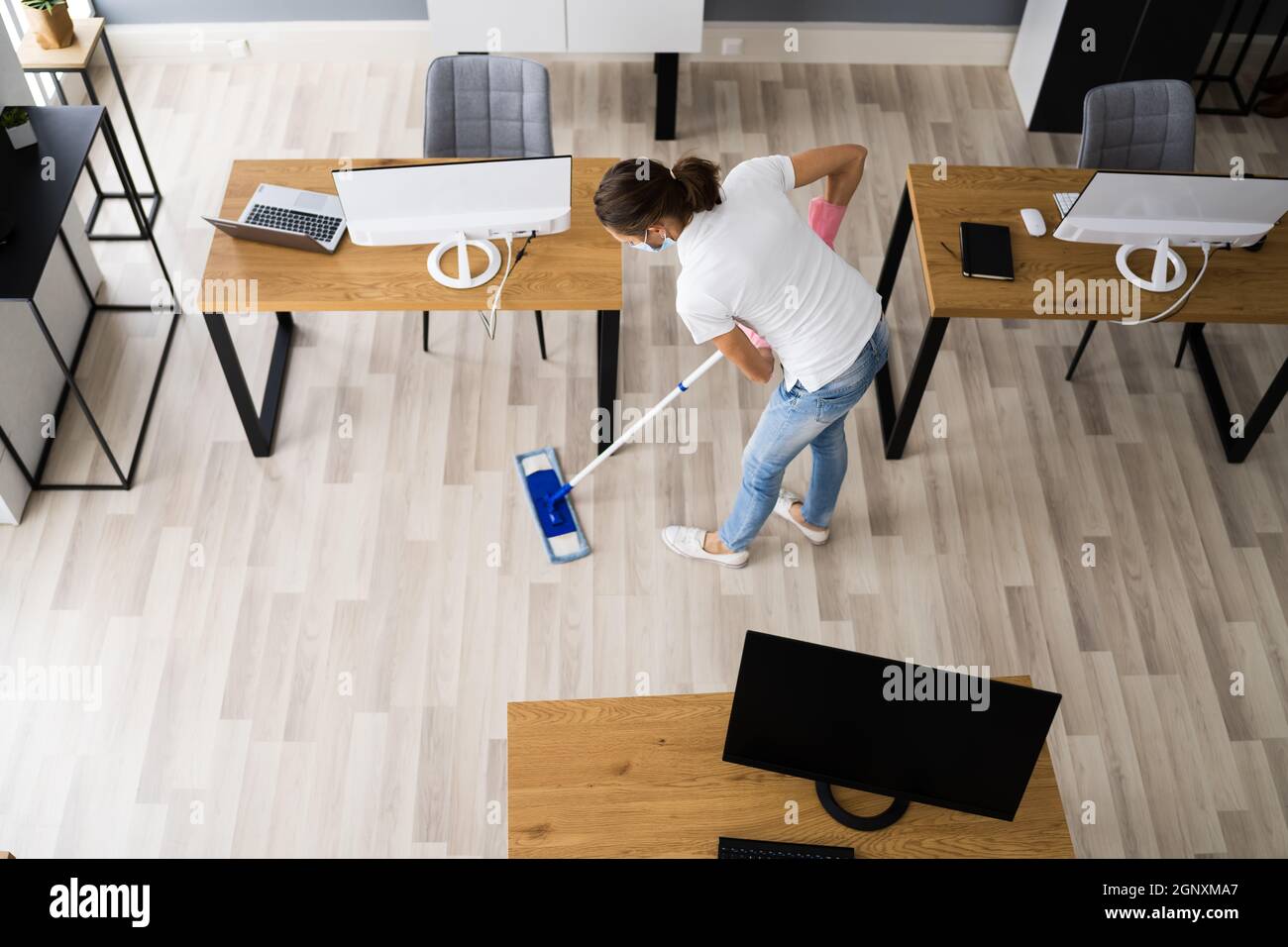 Female Janitor Mopping Floor In Face Mask In Office Stock Photo