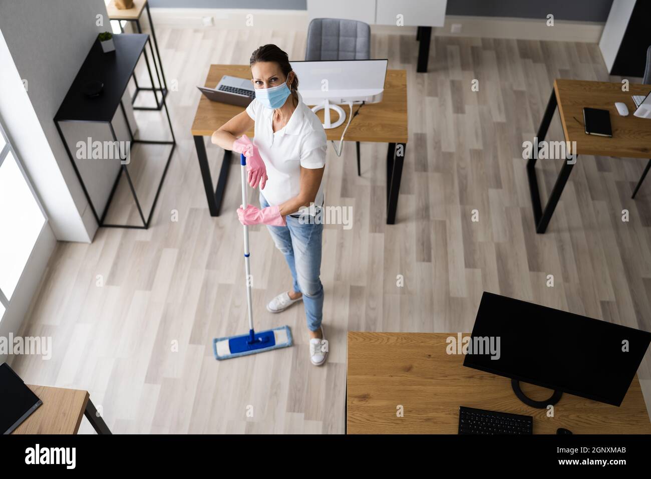 Female Janitor Mopping Floor In Face Mask In Office Stock Photo