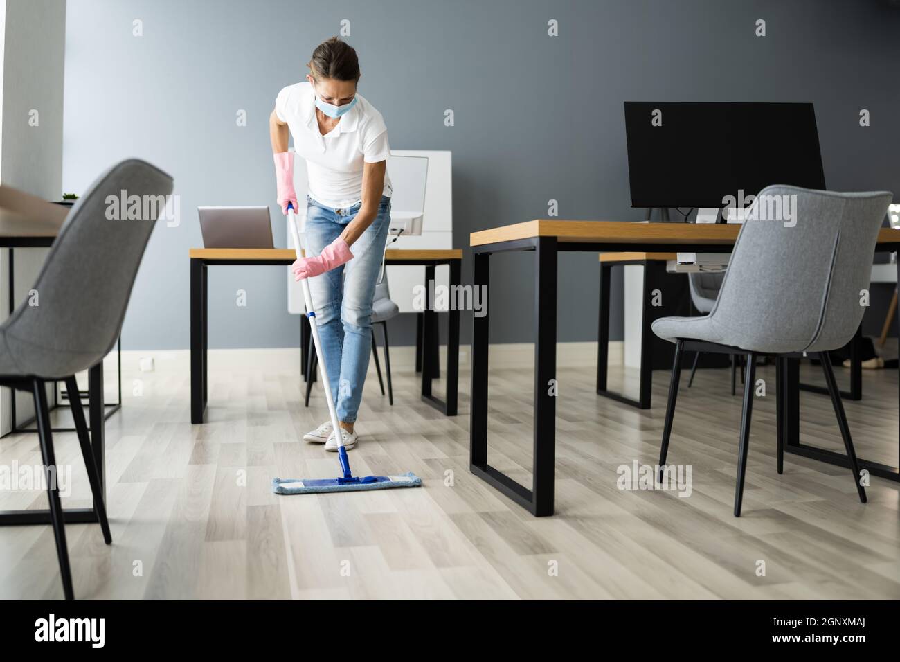 Female Janitor Mopping Floor In Face Mask In Office Stock Photo