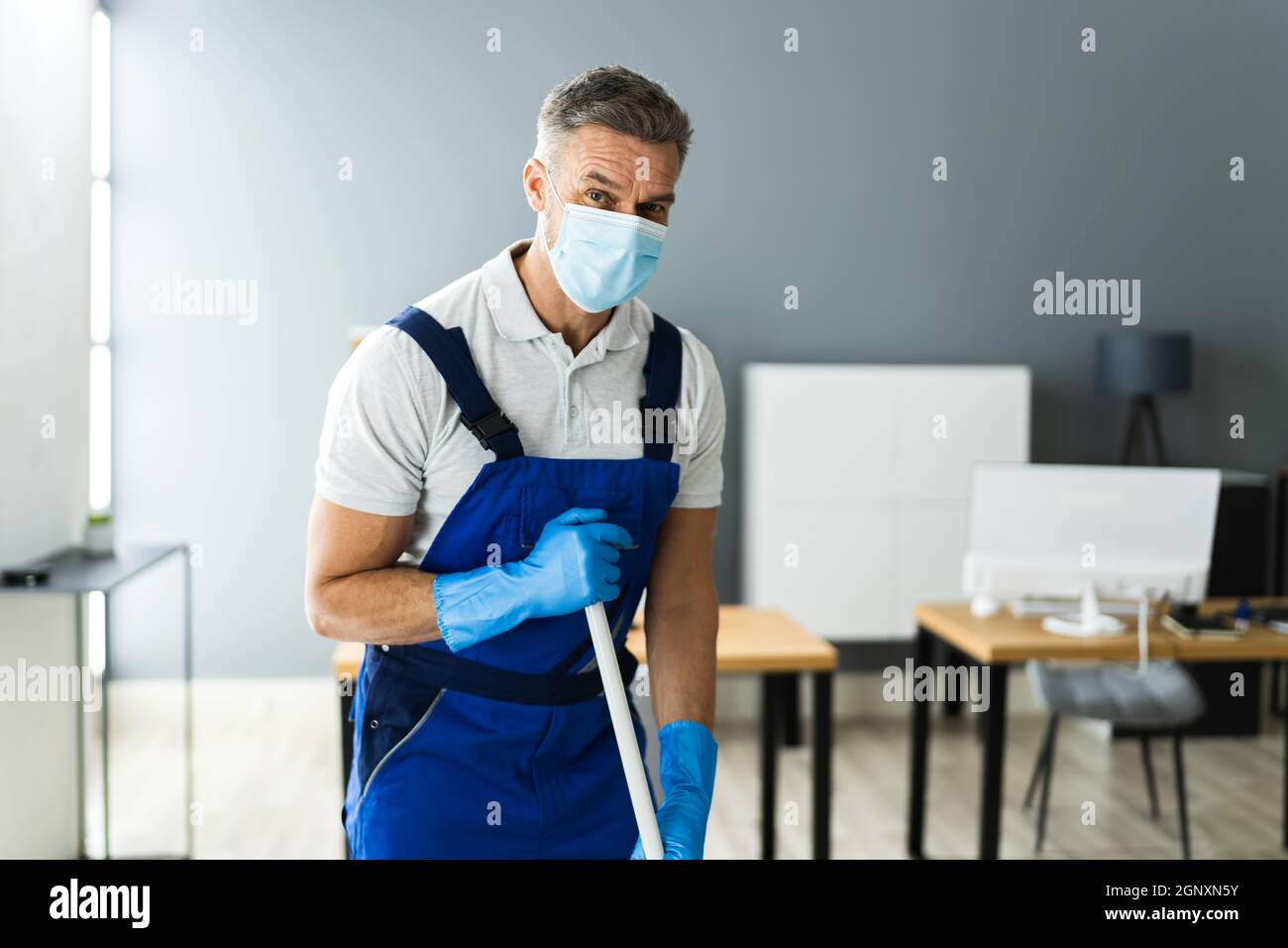 Male Janitor Mopping Floor In Face Mask In Office Stock Photo