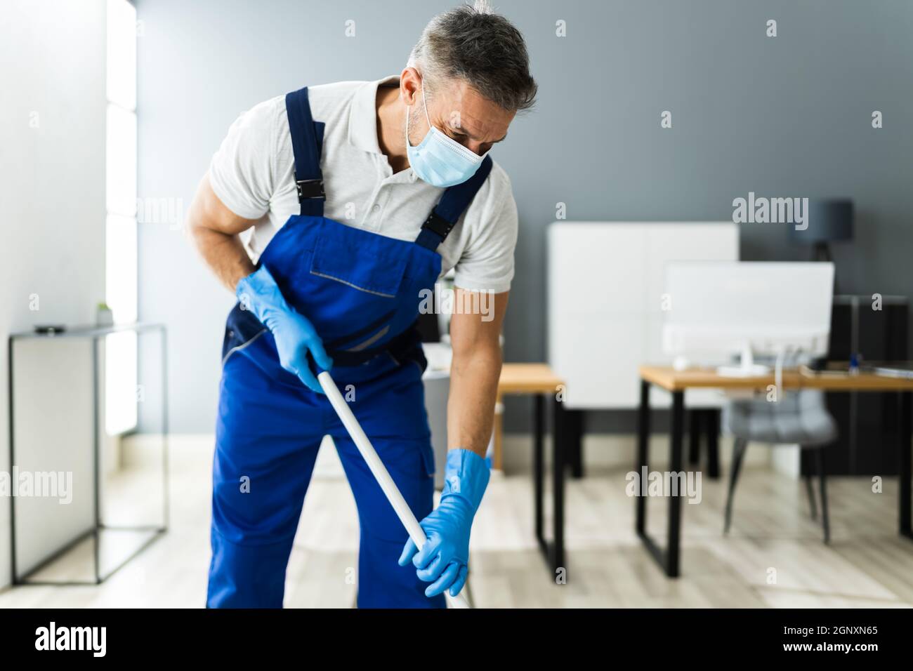 Male Janitor Mopping Floor In Face Mask In Office Stock Photo