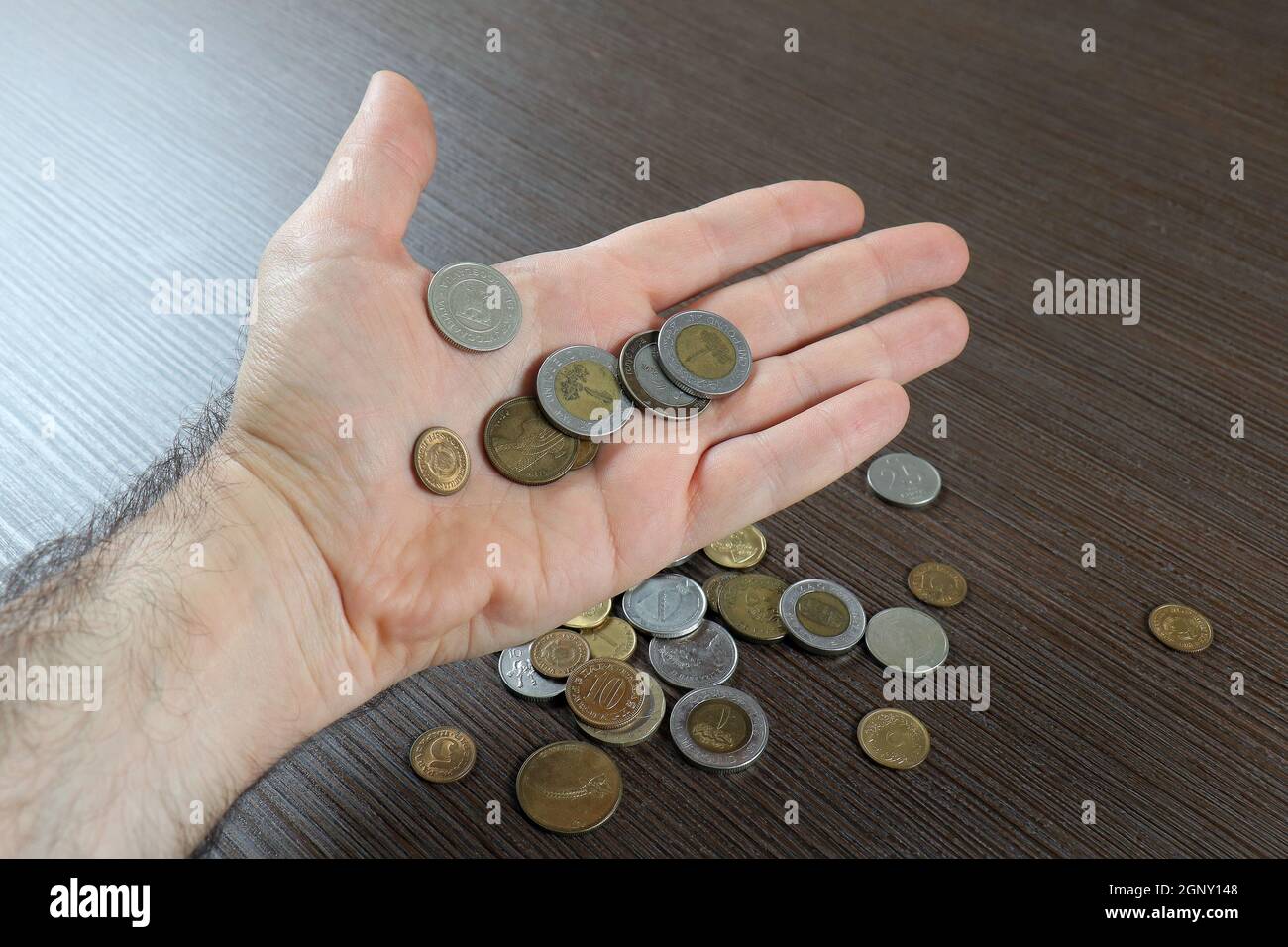 Male hand holding several international currencies coins with more on wooden background Stock Photo
