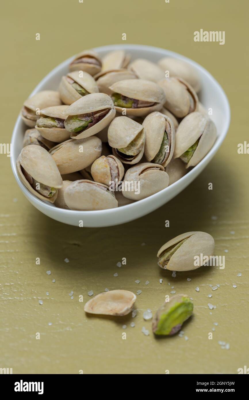 Pistachio nuts in bowl on green wooden background. Stock Photo