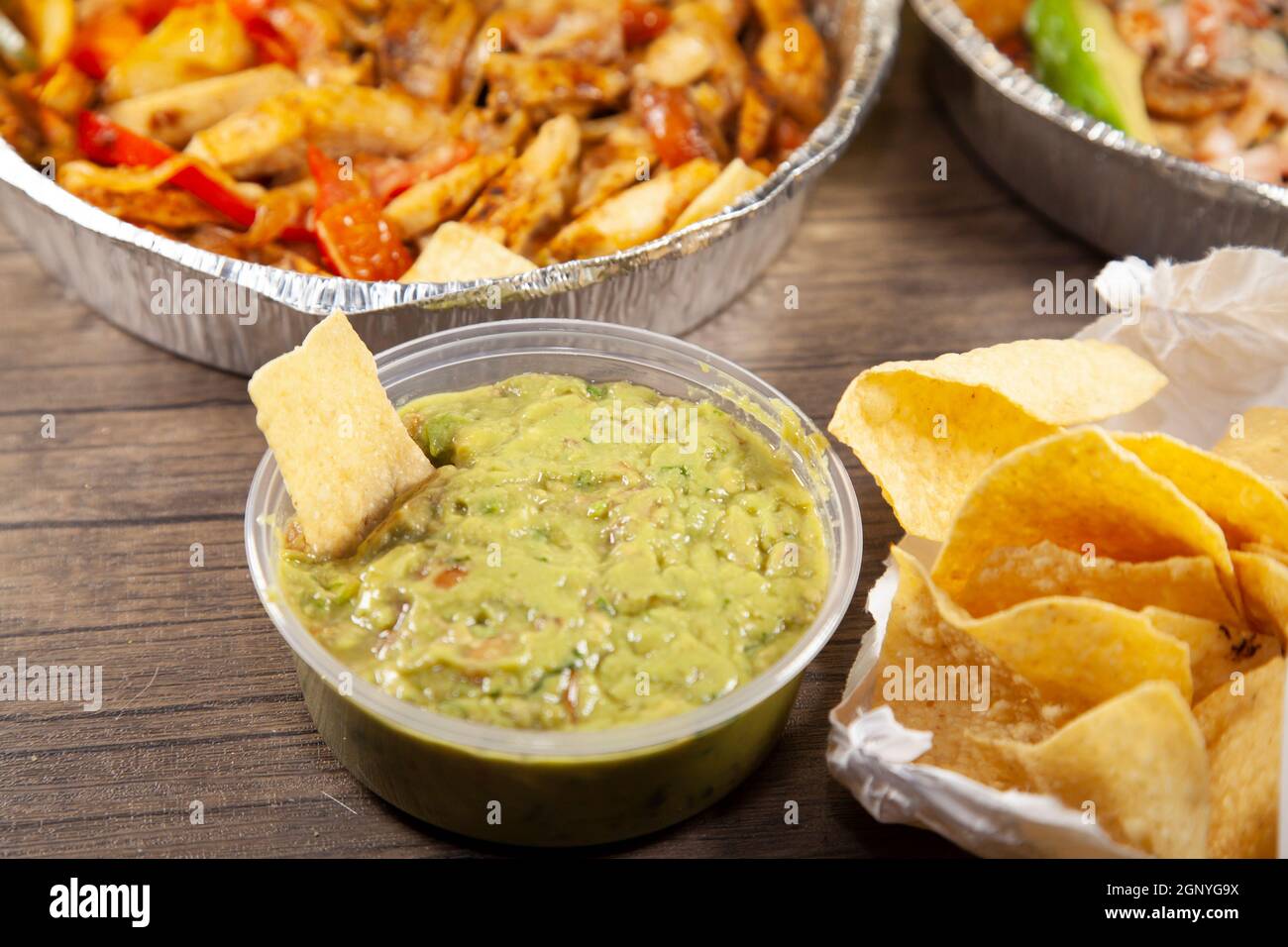 Tortilla chip in guacamole next to an open bag of chips and two takeout