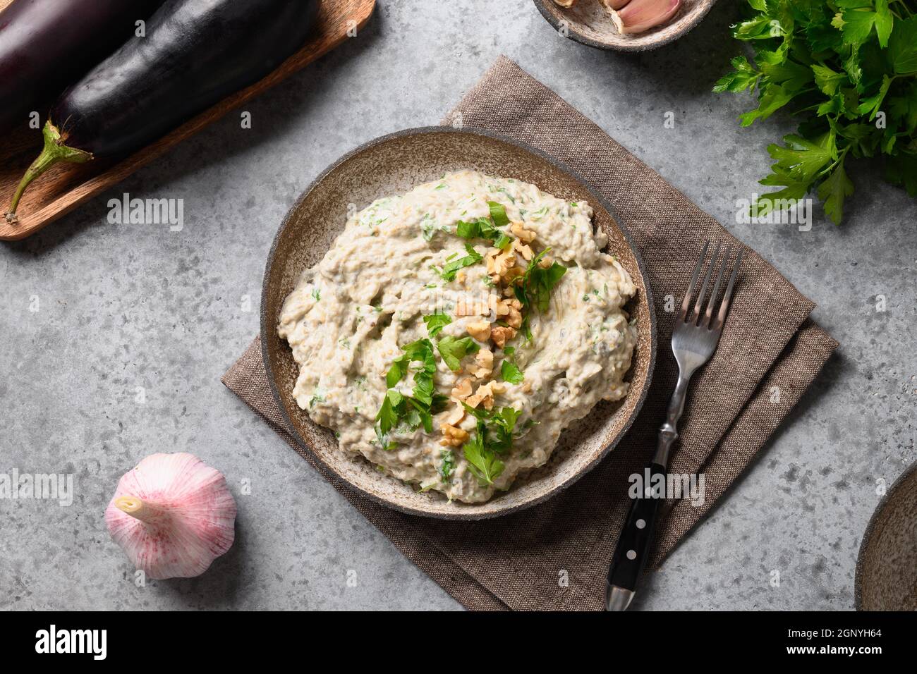 Baba ganoush appetizer from baked eggplant with fresh parsley, walnuts, garlic and olive oil on gray background. Arabic and lebanese cuisine. View fro Stock Photo