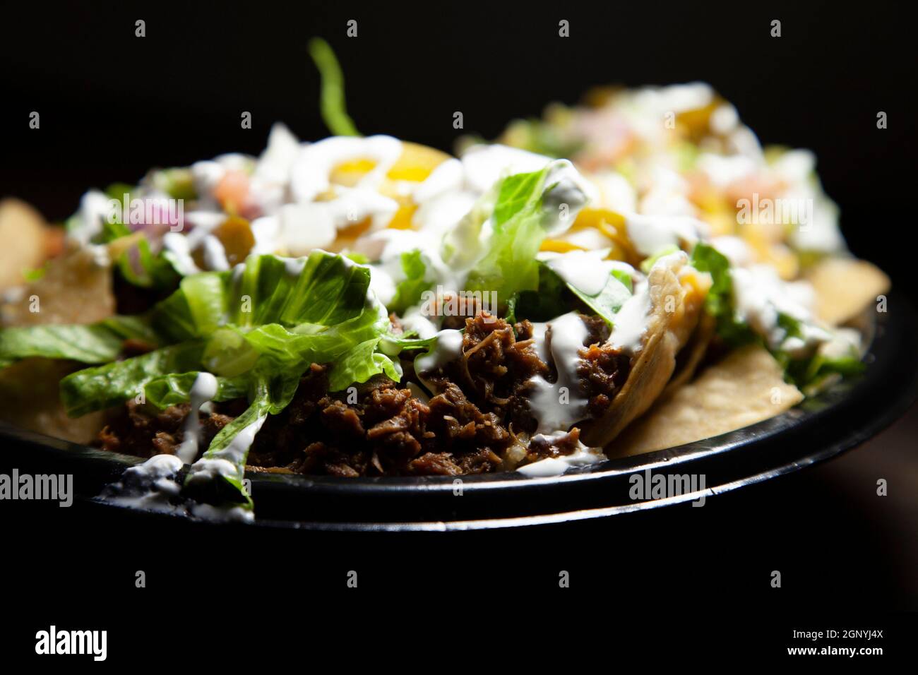 Nachos covered with shredded steak and lettuce, sliced jalapenos, sour