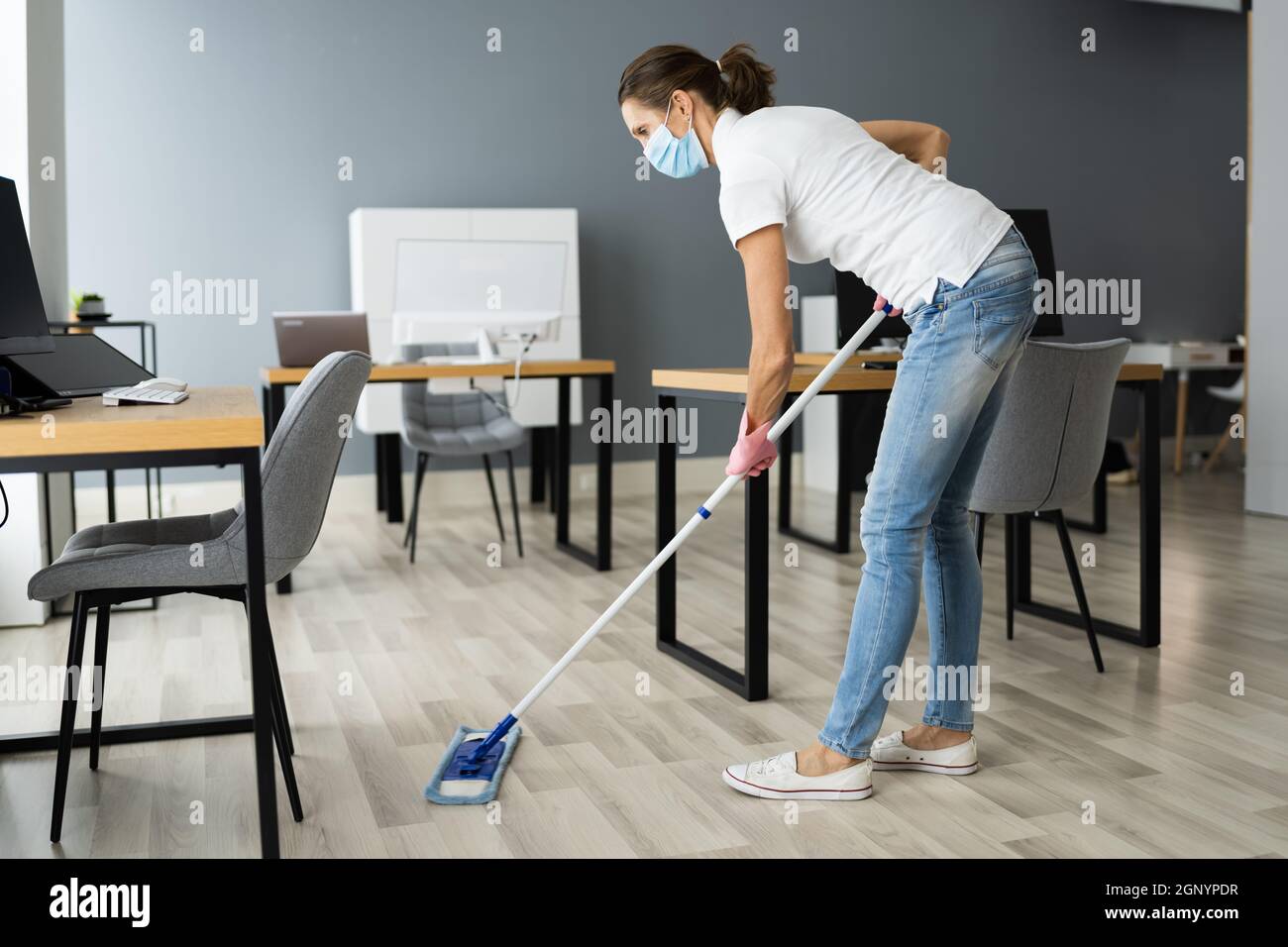 Female Janitor Mopping Floor In Face Mask In Office Stock Photo