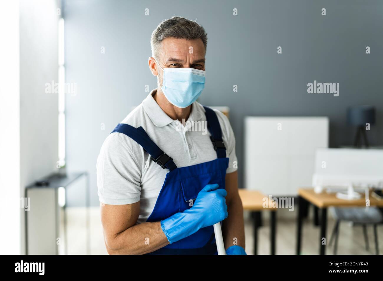 Male Janitor Mopping Floor In Face Mask In Office Stock Photo