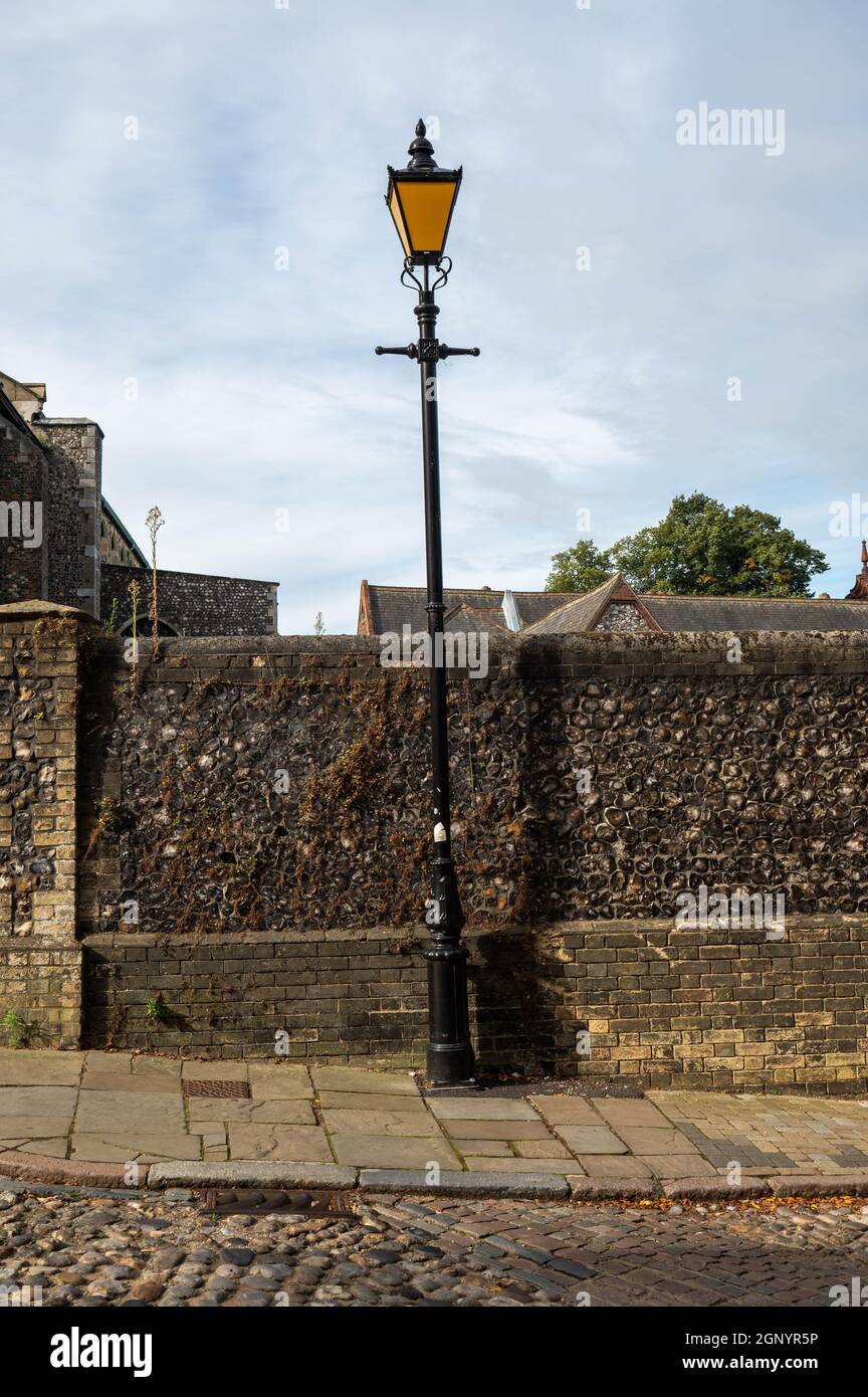 An old fashoned tall black lamp post next to an old flint wall on a