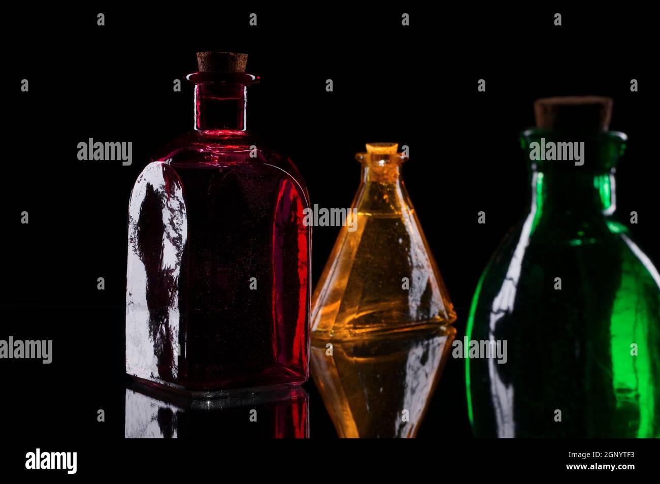 Still life of three colored decorative bottles with corks on glass against black background. Stock Photo