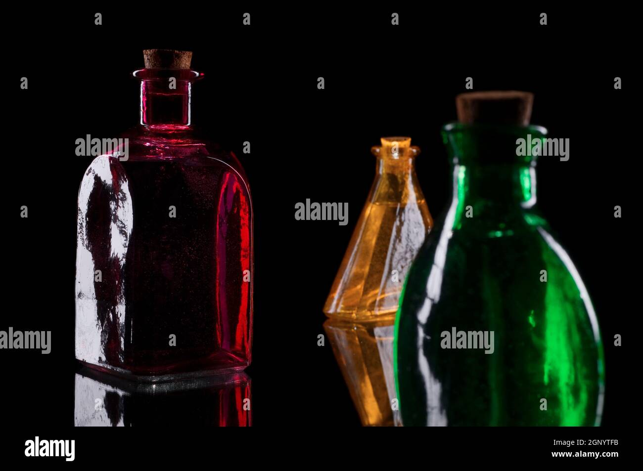 Still life of three colored decorative bottles with corks on glass against black background. Stock Photo