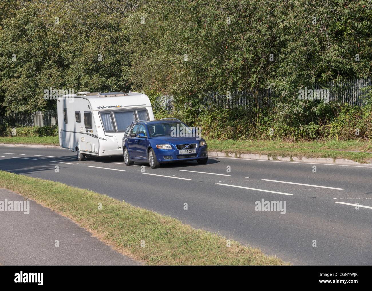 Blue Volvo car towing Expression 540 caravan travelling uphill on country road in Cornwall. For UK caravans, staycations in UK, alternative holidays. Stock Photo